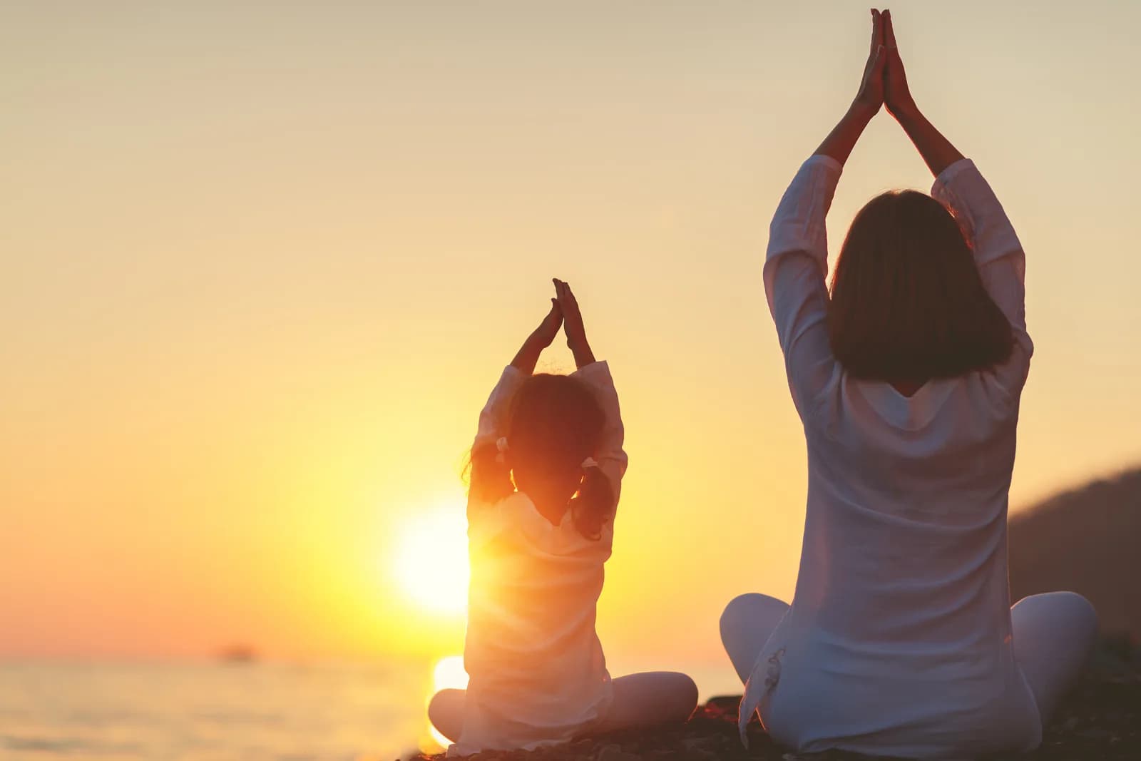 Mère et fille pratiquant la méditation de pleine conscience face à un coucher de soleil. Programme Mindful UP enfants